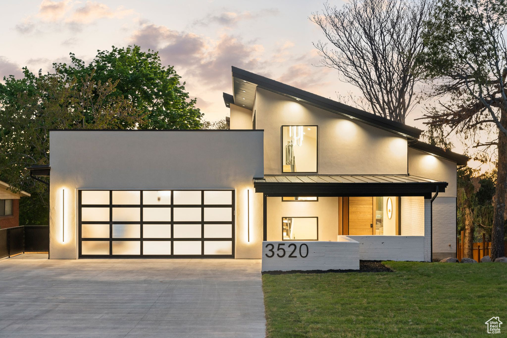 Modern home with a garage, metal roof, concrete driveway, a front lawn, and a standing seam roof