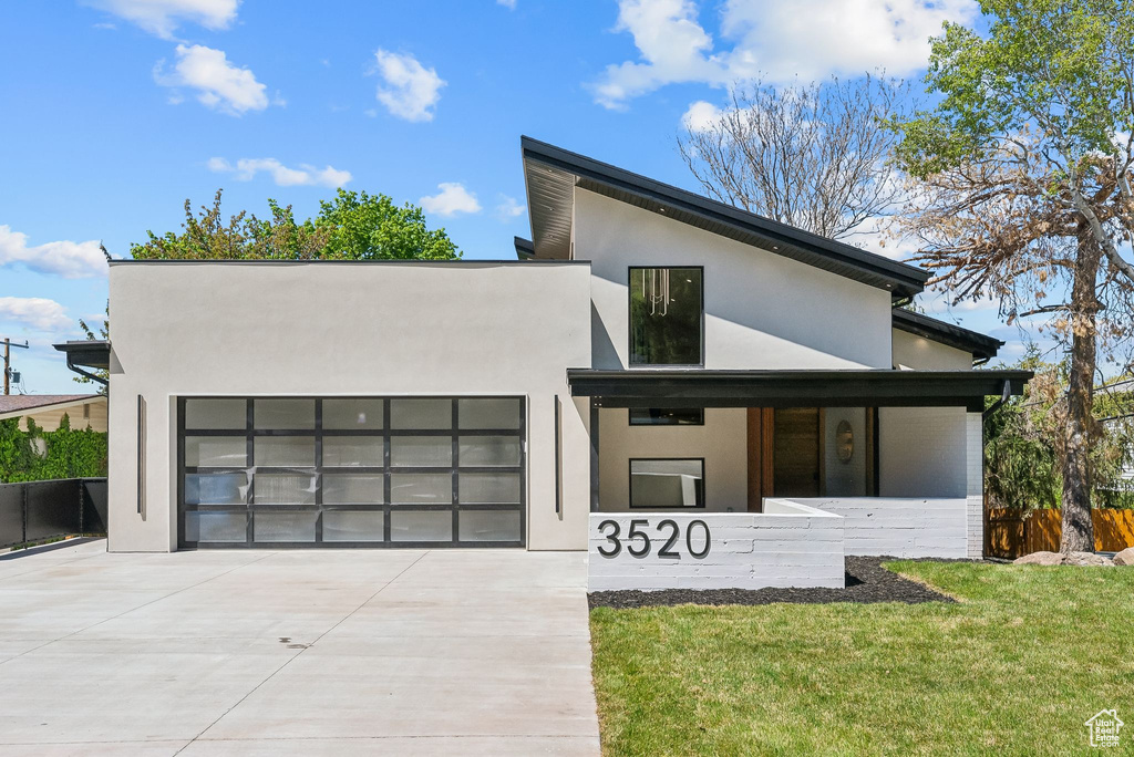 Contemporary home with covered porch, a garage, stucco siding, concrete driveway, and a front yard