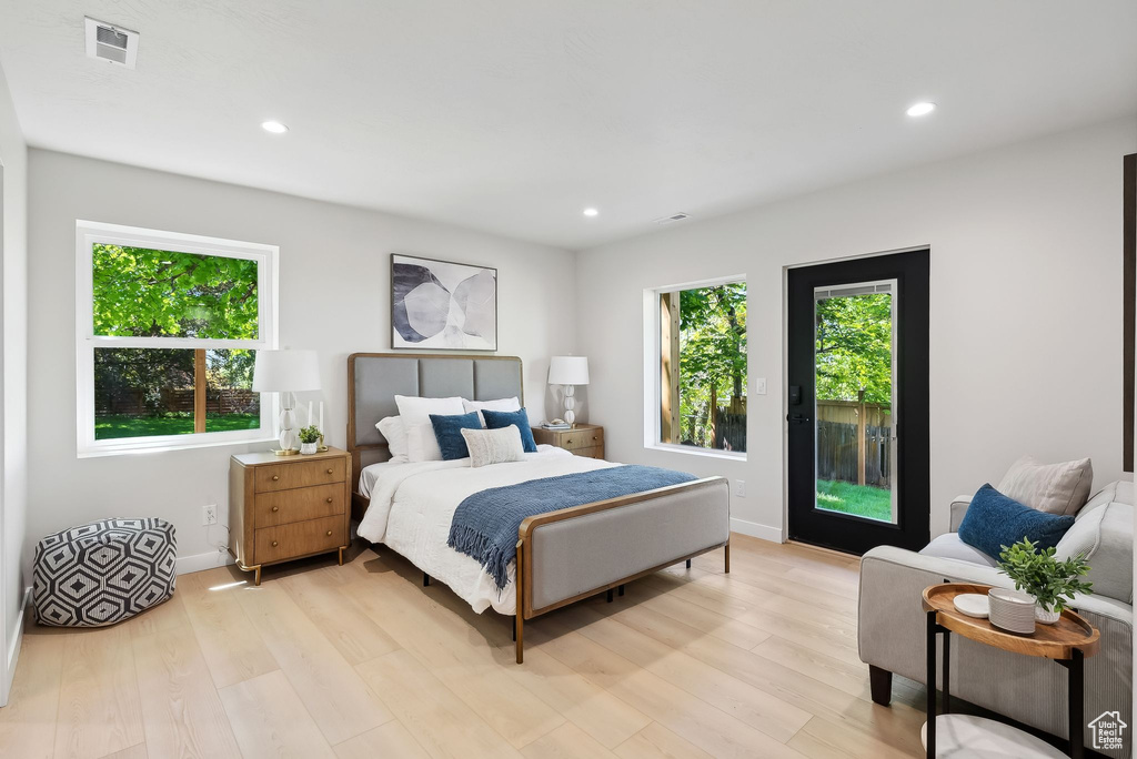 Bedroom with light wood-type flooring, access to exterior, visible vents, and multiple windows