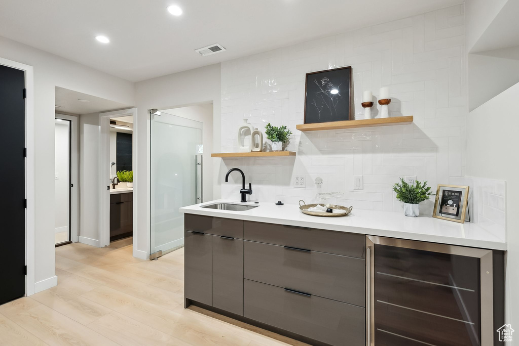Bar with a sink, visible vents, light wood-style floors, decorative backsplash, and wine cooler