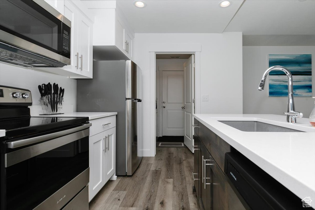 Kitchen with light countertops, white cabinets, a sink, light wood-style flooring, and appliances with stainless steel finishes