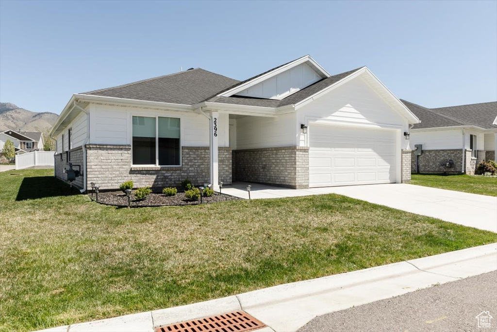View of front of home featuring board and batten siding, a front yard, a garage, brick siding, and concrete driveway