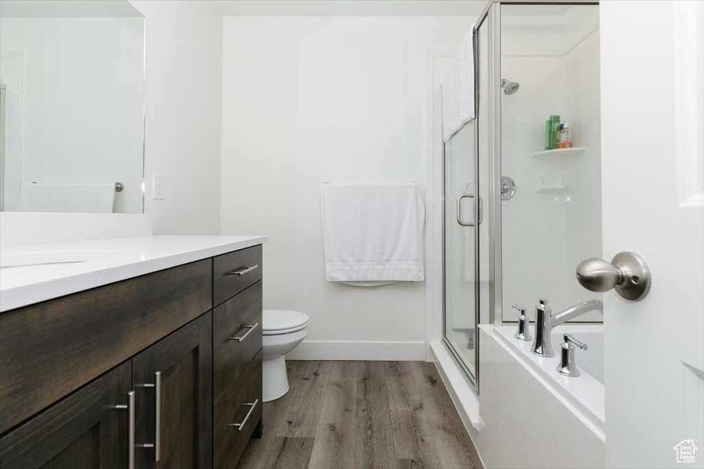 Bathroom featuring a washtub, a shower with shower door, wood finished floors, vanity, and toilet
