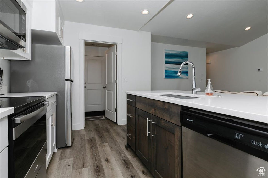 Kitchen with dark brown cabinetry, a sink, light countertops, light wood-style floors, and stainless steel appliances