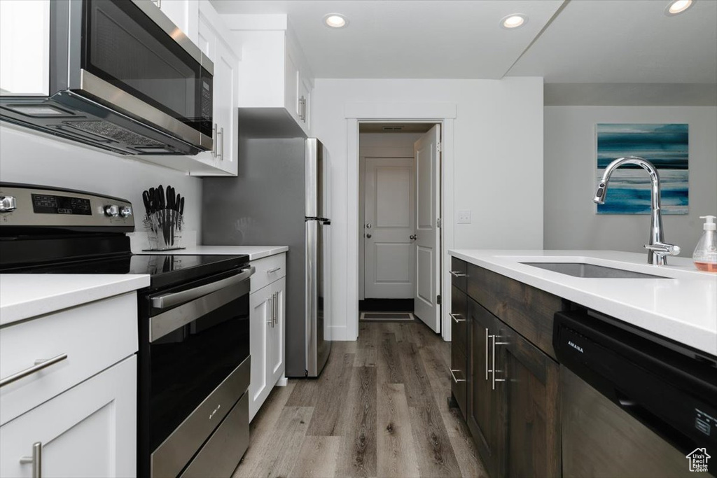 Kitchen featuring white cabinets, appliances with stainless steel finishes, a sink, and light wood-type flooring