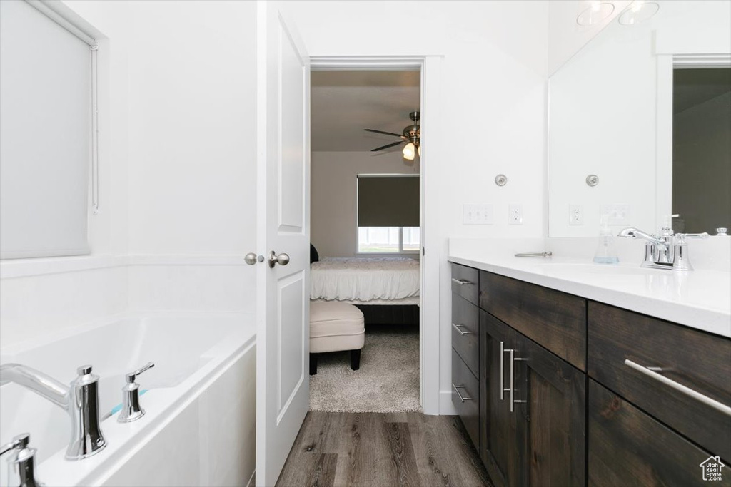 Bathroom with connected bathroom, wood finished floors, a garden tub, and vanity