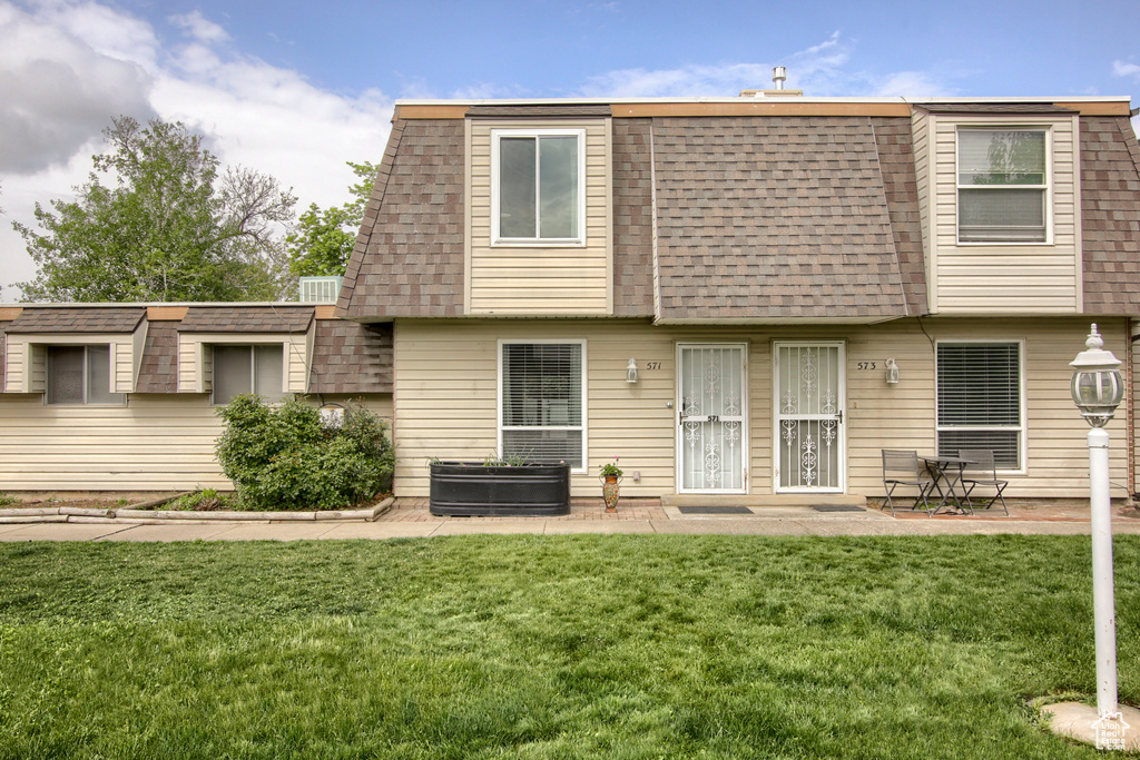 Rear view of house featuring roof with shingles, mansard roof, a lawn, and a patio area