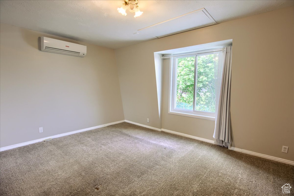 Empty room with an AC wall unit, attic access, baseboards, and carpet