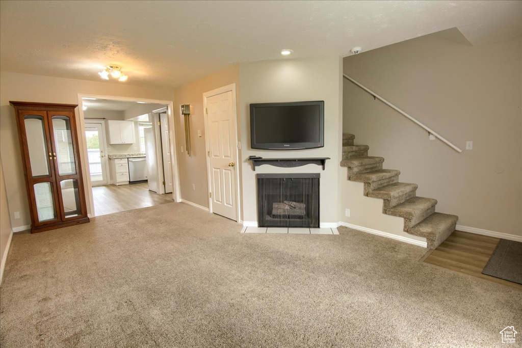 Unfurnished living room with stairway, light colored carpet, baseboards, and a fireplace with flush hearth