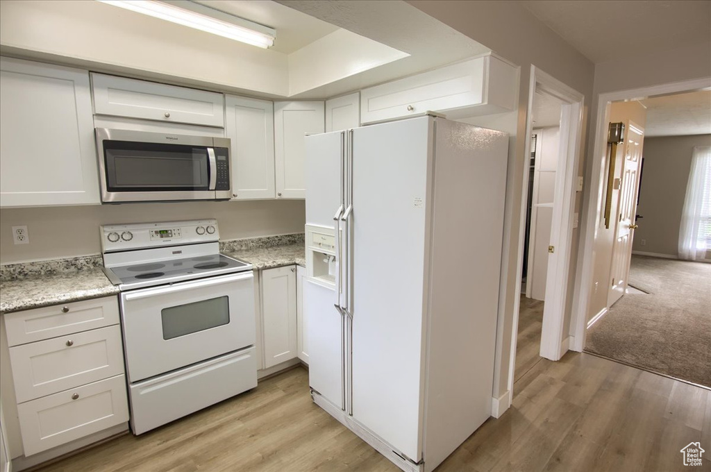 Kitchen featuring white appliances, light wood-type flooring, and white cabinets