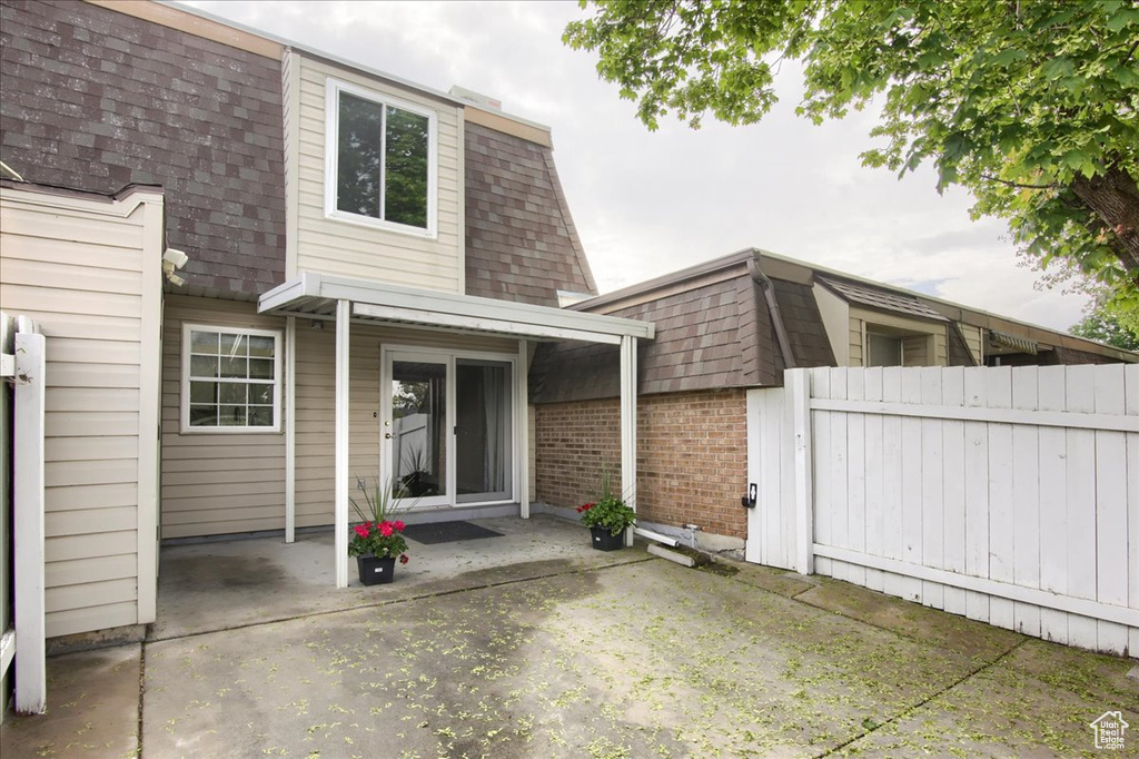 Exterior space with mansard roof, fence, brick siding, roof with shingles, and a patio area