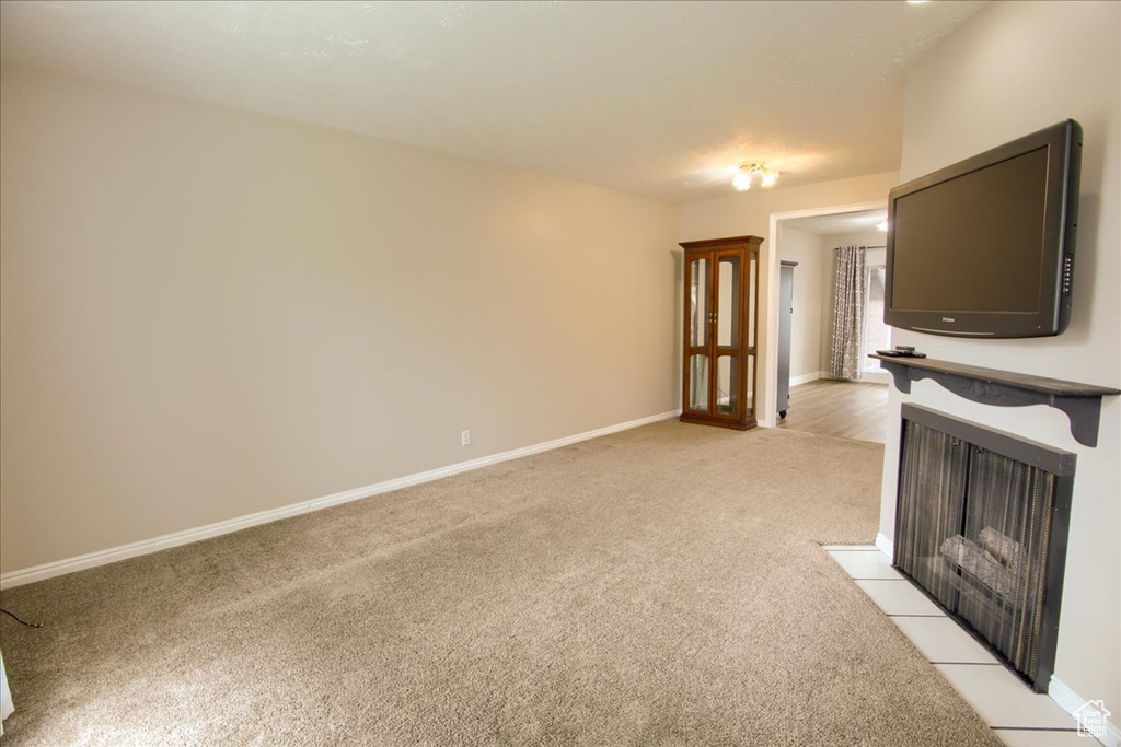 Unfurnished living room with baseboards, light carpet, and a fireplace with flush hearth