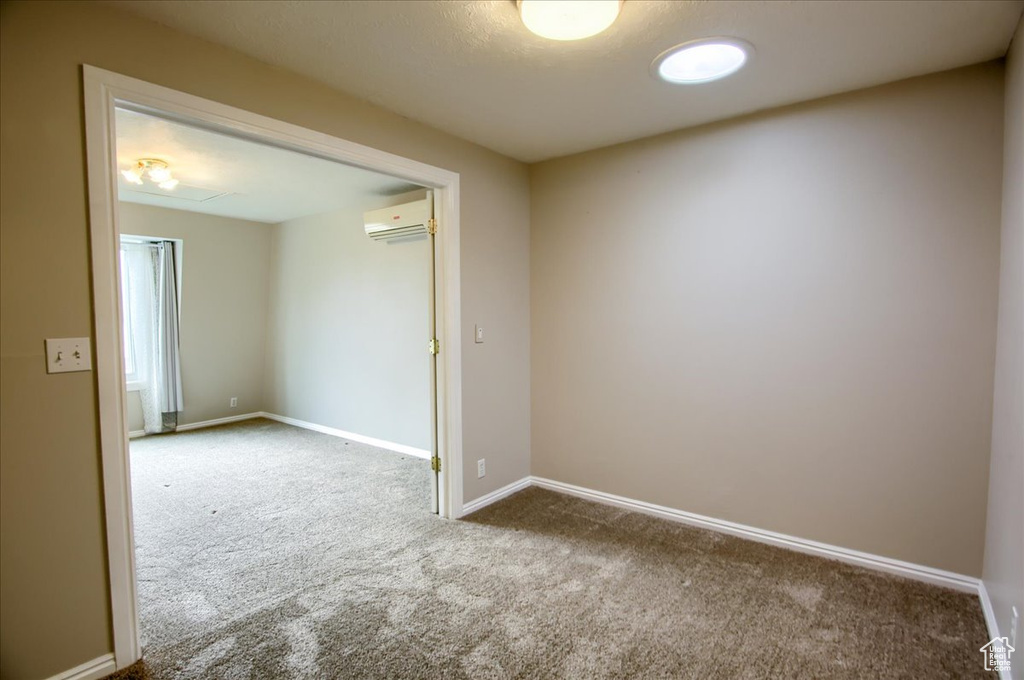 Empty room with baseboards, a wall unit AC, and carpet floors