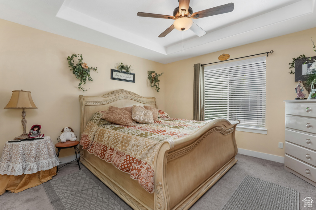 Carpeted bedroom featuring ceiling fan, a raised ceiling, and baseboards