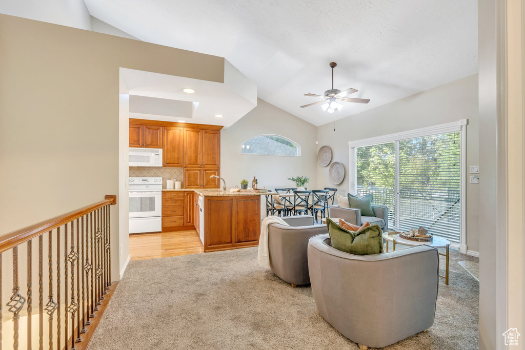 Living room featuring vaulted ceiling, ceiling fan, and light carpet
