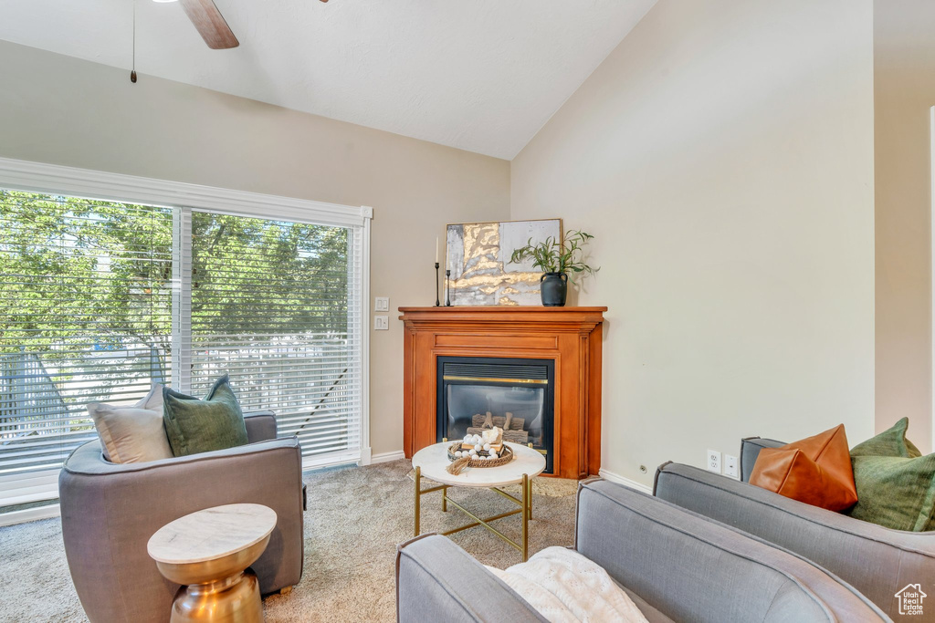 Living area featuring carpet, baseboards, ceiling fan, a glass covered fireplace, and vaulted ceiling