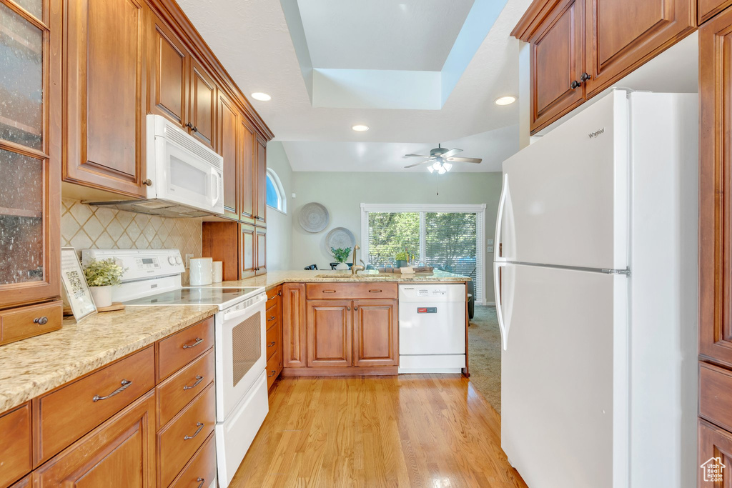 Kitchen with a peninsula, light wood finished floors, a sink, white appliances, and recessed lighting