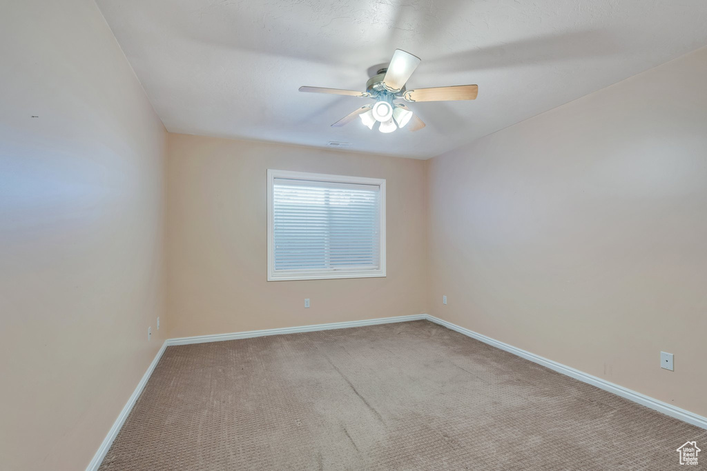 Carpeted empty room featuring baseboards and a ceiling fan