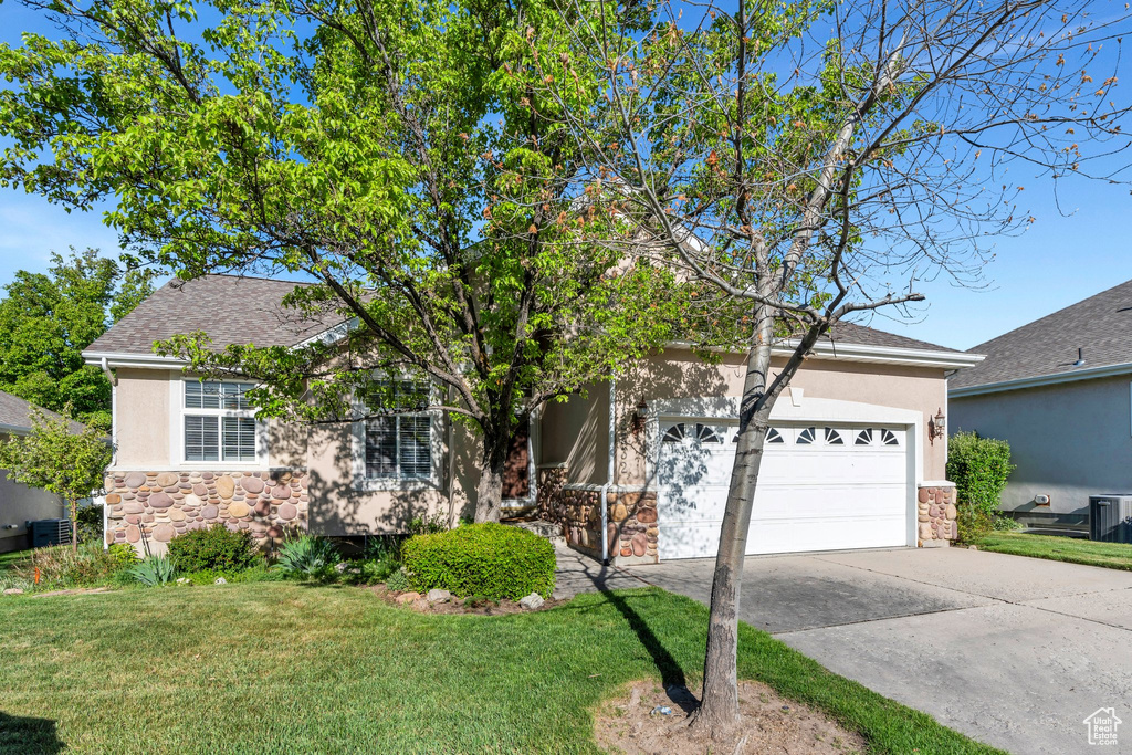 Obstructed view of property featuring a garage, stucco siding, concrete driveway, stone siding, and a front lawn