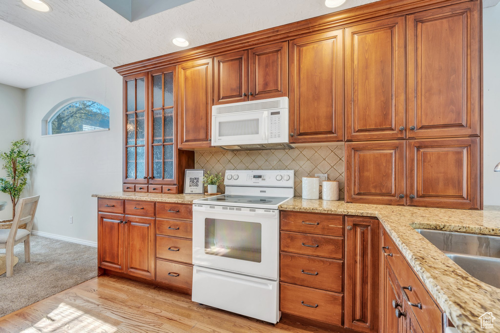 Kitchen with brown cabinets, white appliances, tasteful backsplash, and a sink