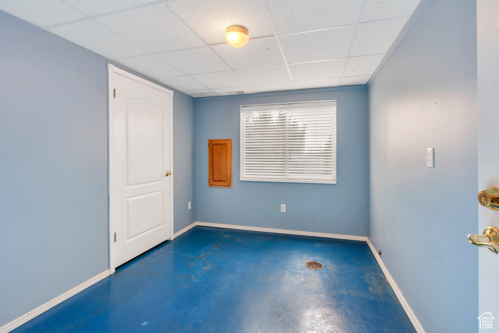 Empty room featuring baseboards, a paneled ceiling, and finished concrete floors