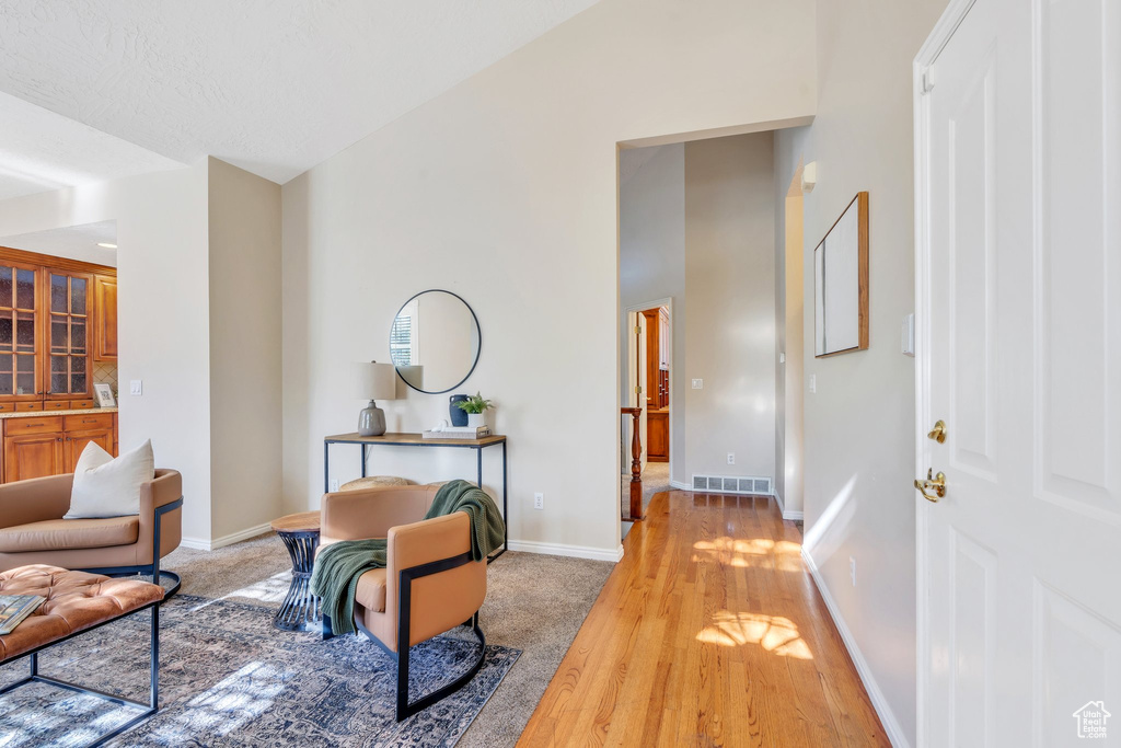 Hall featuring baseboards, light wood finished floors, visible vents, and high vaulted ceiling