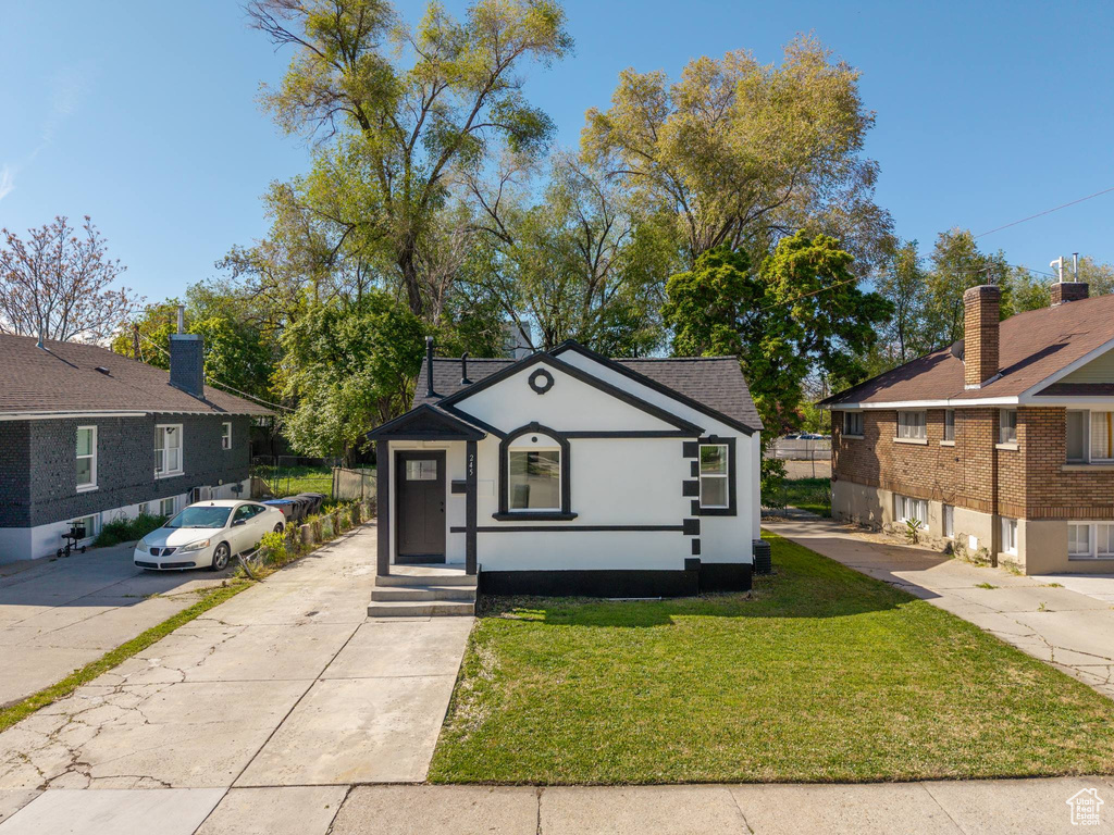 Bungalow-style house with driveway, stucco siding, a shingled roof, and a front lawn
