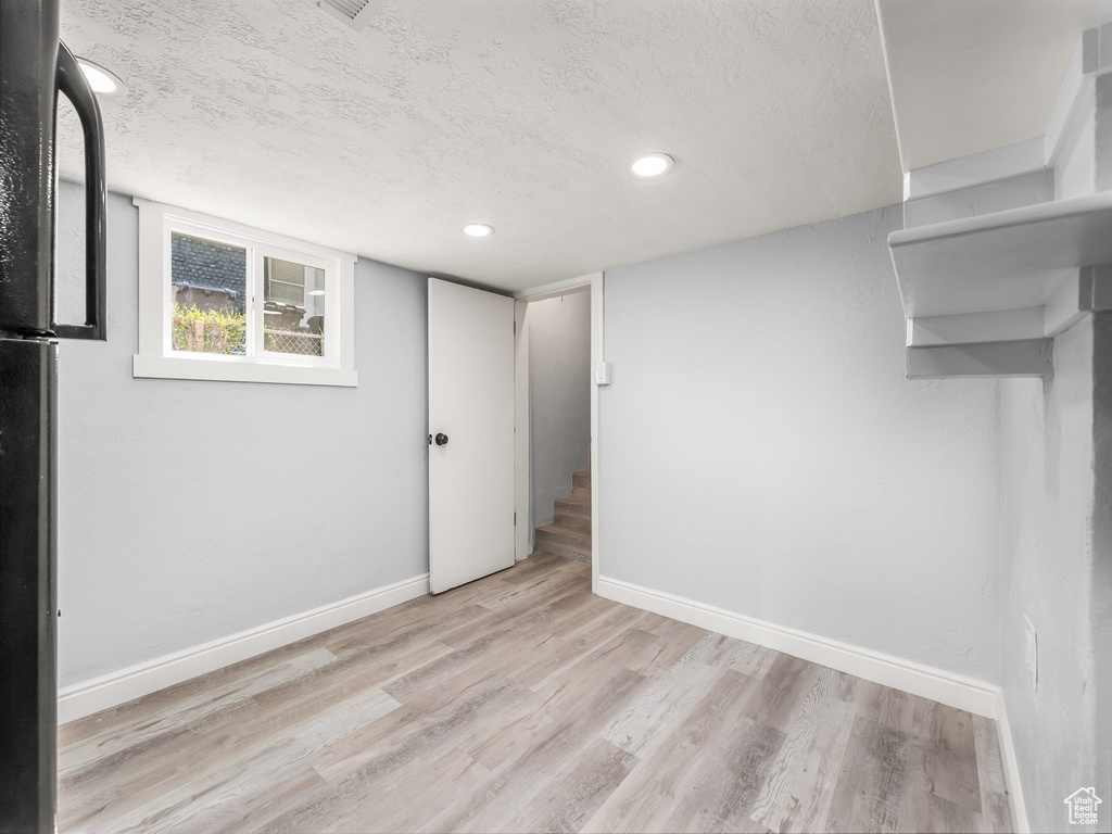 Below grade area with baseboards, light wood-type flooring, and a textured ceiling