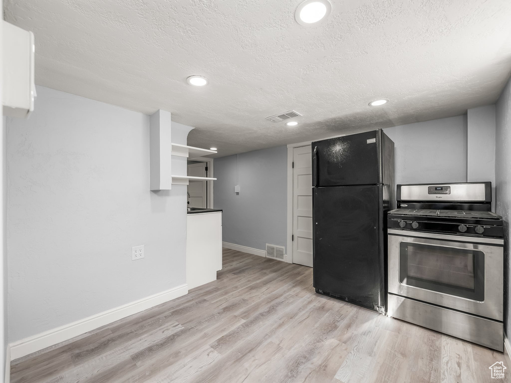 Kitchen featuring freestanding refrigerator, a textured ceiling, gas range, and visible vents