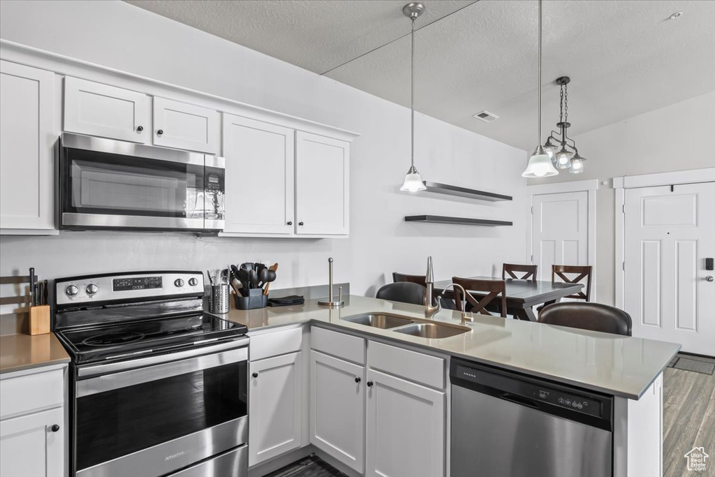 Kitchen featuring a peninsula, wood finished floors, visible vents, white cabinets, and appliances with stainless steel finishes