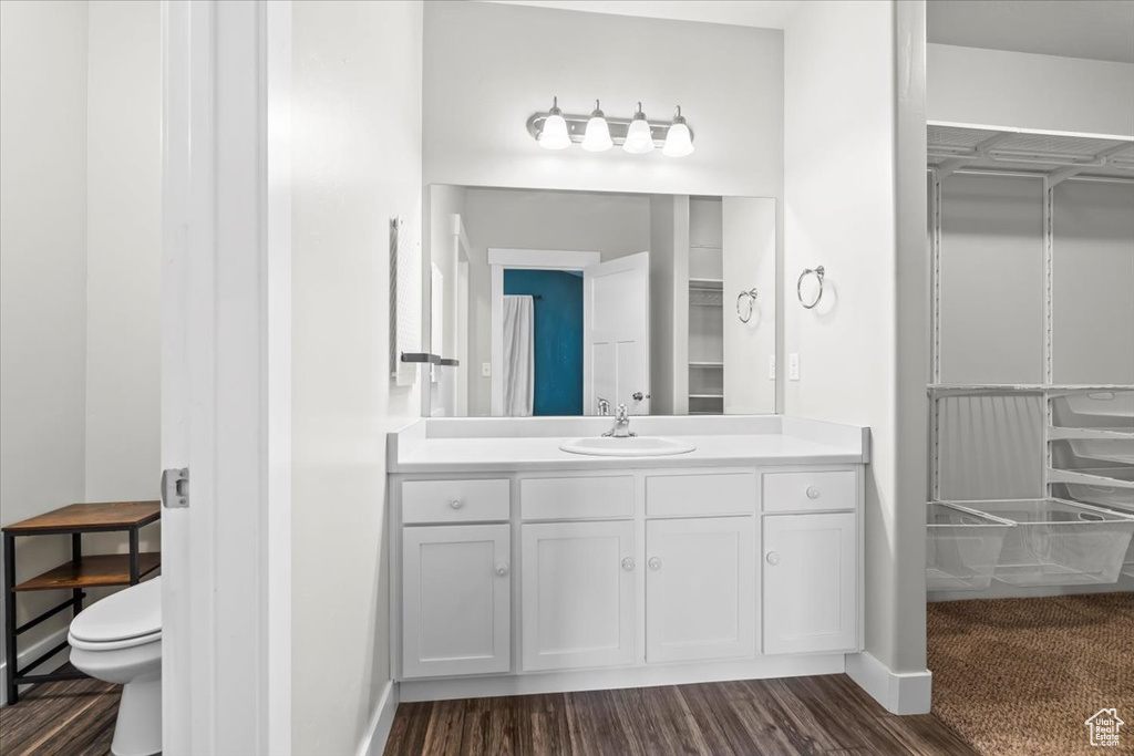 Full bathroom with toilet, wood finished floors, vanity, a walk in closet, and baseboards