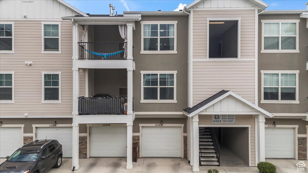 Townhome / multi-family property with a balcony, board and batten siding, a garage, and driveway