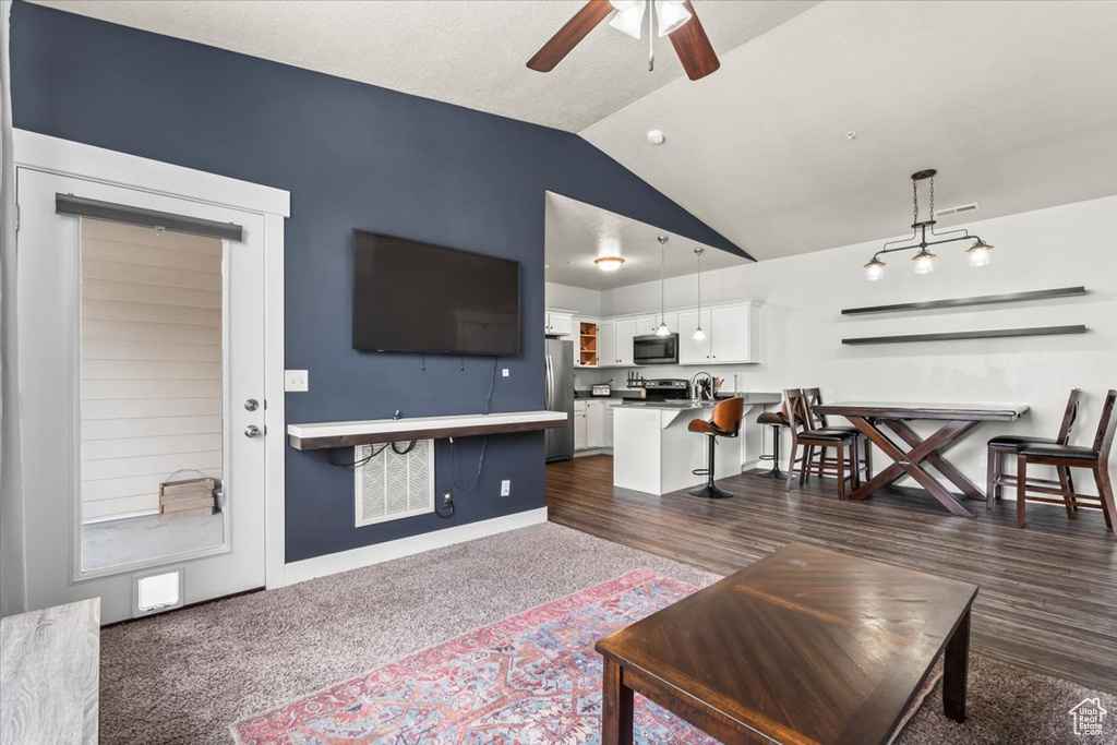 Living area with vaulted ceiling, ceiling fan, baseboards, and dark carpet