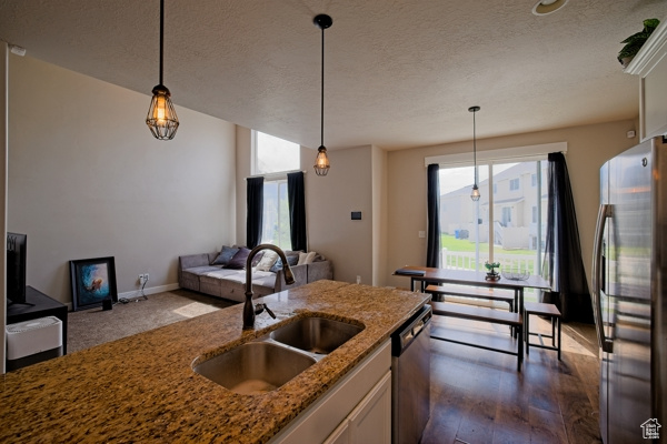 Kitchen featuring stone countertops, stainless steel appliances, a sink, and decorative light fixtures