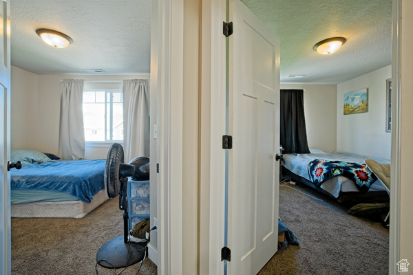 Bedroom with a textured ceiling, carpet floors, and visible vents