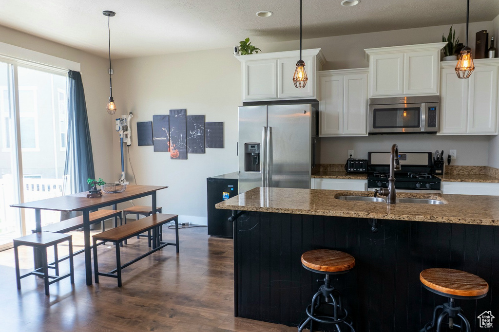 Kitchen featuring appliances with stainless steel finishes, dark wood finished floors, light stone countertops, white cabinets, and a kitchen breakfast bar