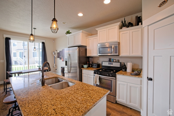 Kitchen with wood finished floors, a sink, stainless steel appliances, white cabinets, and a kitchen island with sink