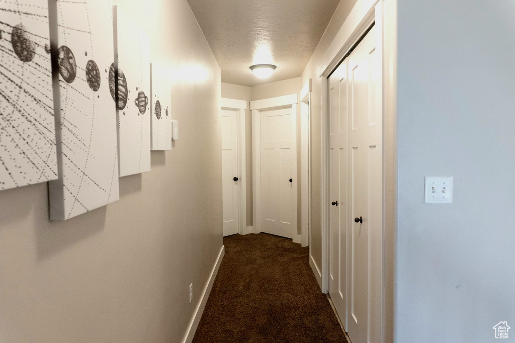 Corridor featuring baseboards and dark colored carpet