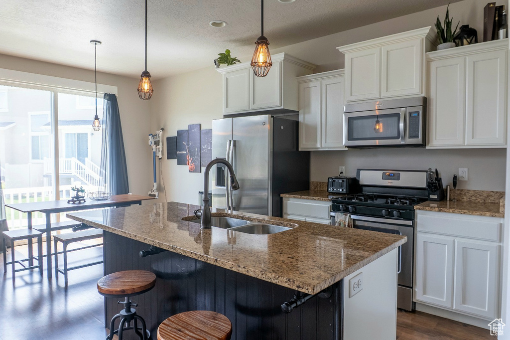 Kitchen featuring stainless steel appliances, white cabinetry, an island with sink, light stone countertops, and a textured ceiling