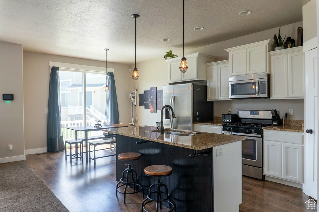 Kitchen featuring appliances with stainless steel finishes, dark wood finished floors, a kitchen island with sink, a kitchen breakfast bar, and white cabinetry