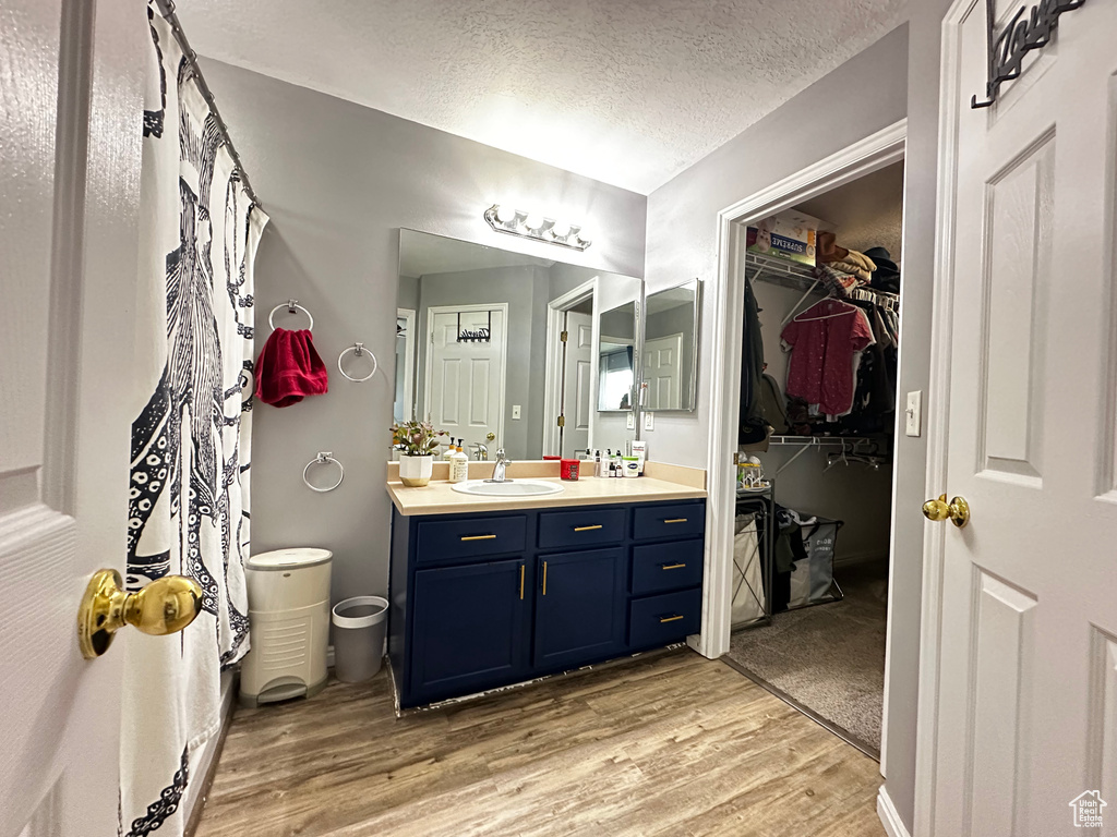 Full bath with a walk in closet, vanity, a textured ceiling, and wood finished floors
