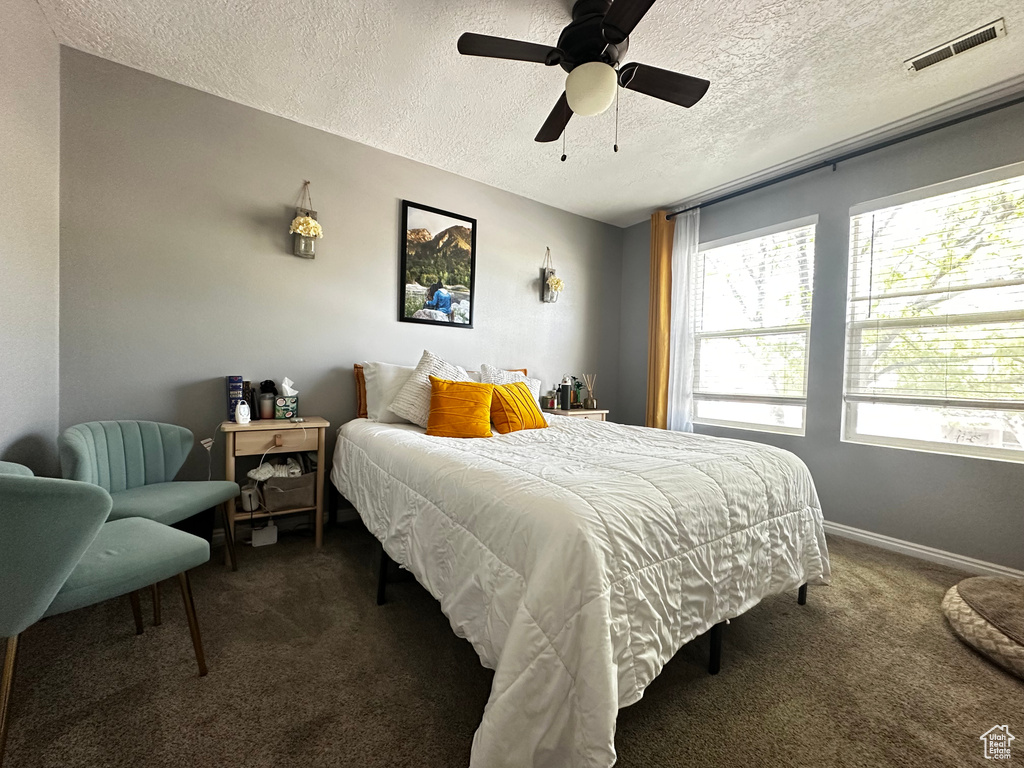 Bedroom featuring dark carpet, a textured ceiling, visible vents, baseboards, and ceiling fan