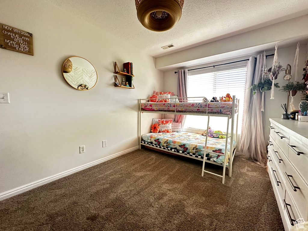 Bedroom with dark colored carpet, a textured ceiling, baseboards, and visible vents