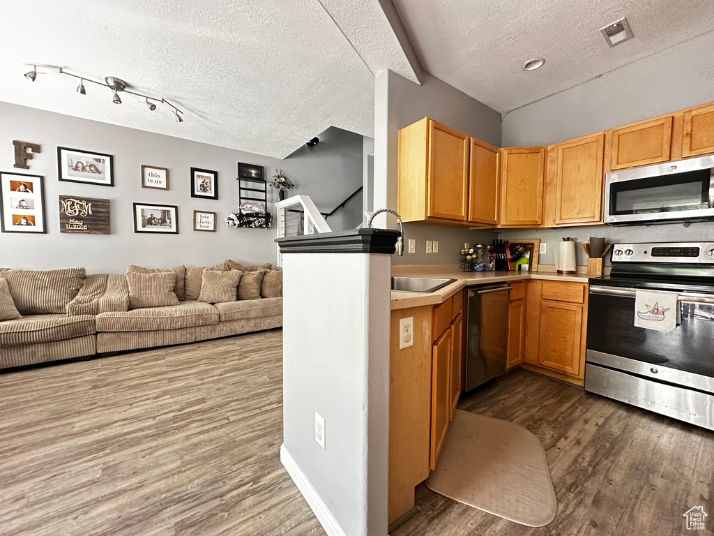 Kitchen with wood finished floors, stainless steel appliances, open floor plan, a textured ceiling, and light countertops