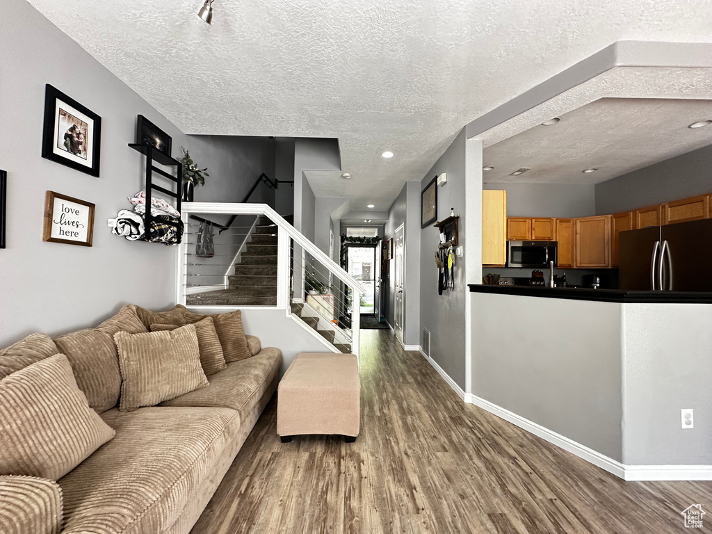 Living room with baseboards, stairs, a textured ceiling, and wood finished floors