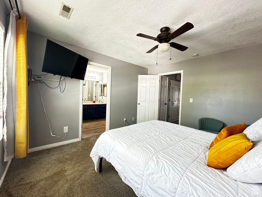 Bedroom featuring a textured ceiling, baseboards, dark colored carpet, visible vents, and connected bathroom