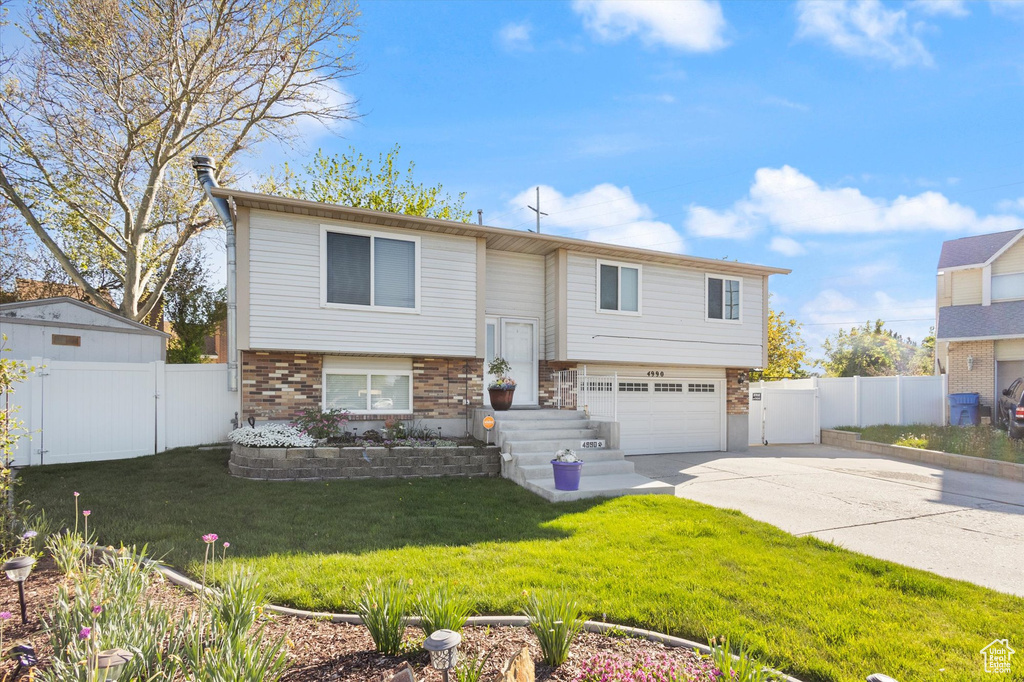 Split foyer home featuring a gate, fence, an attached garage, brick siding, and concrete driveway