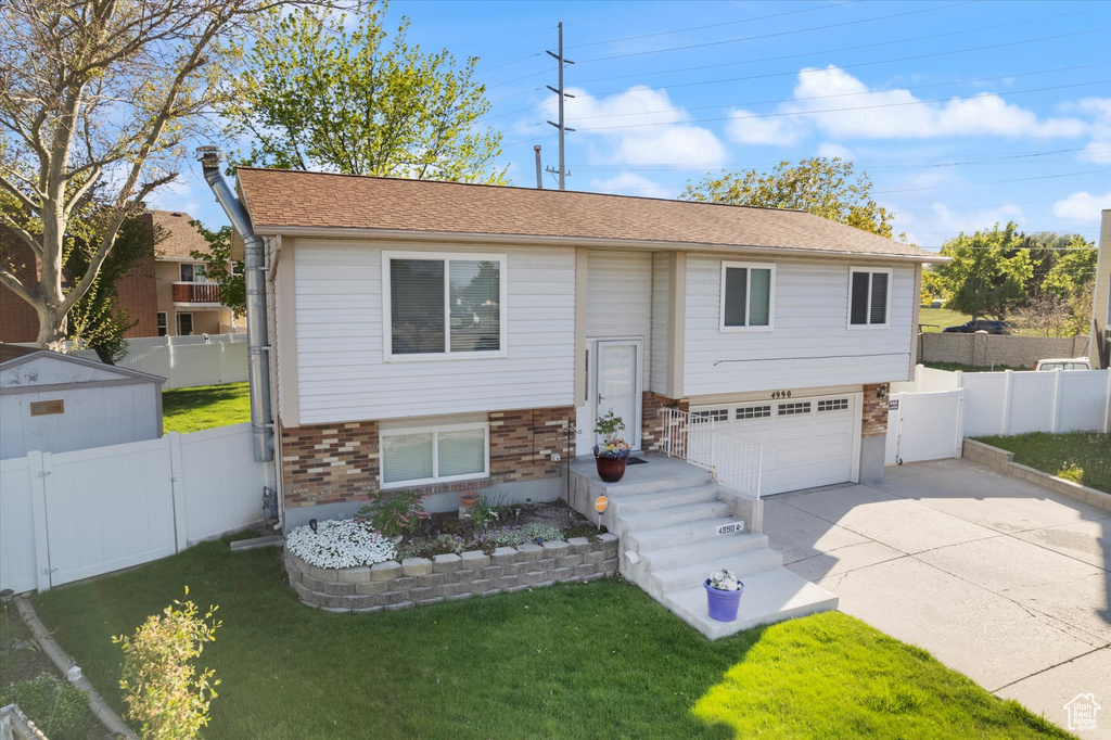 Bi-level home with an attached garage, a gate, concrete driveway, a front yard, and brick siding