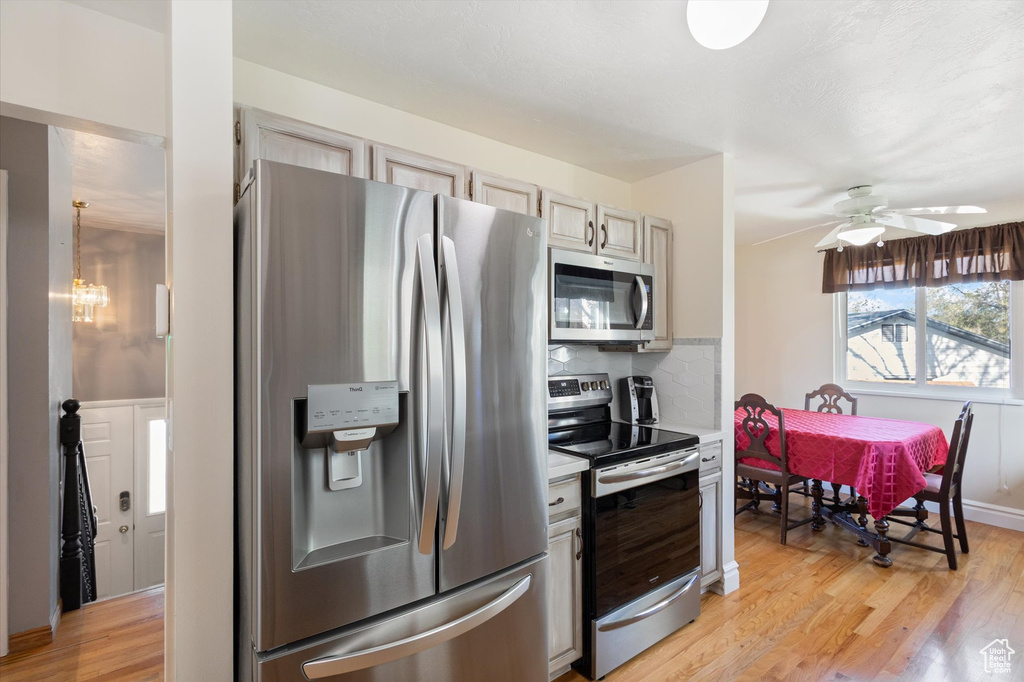 Kitchen with stainless steel appliances, ceiling fan with notable chandelier, light wood-type flooring, light countertops, and decorative backsplash