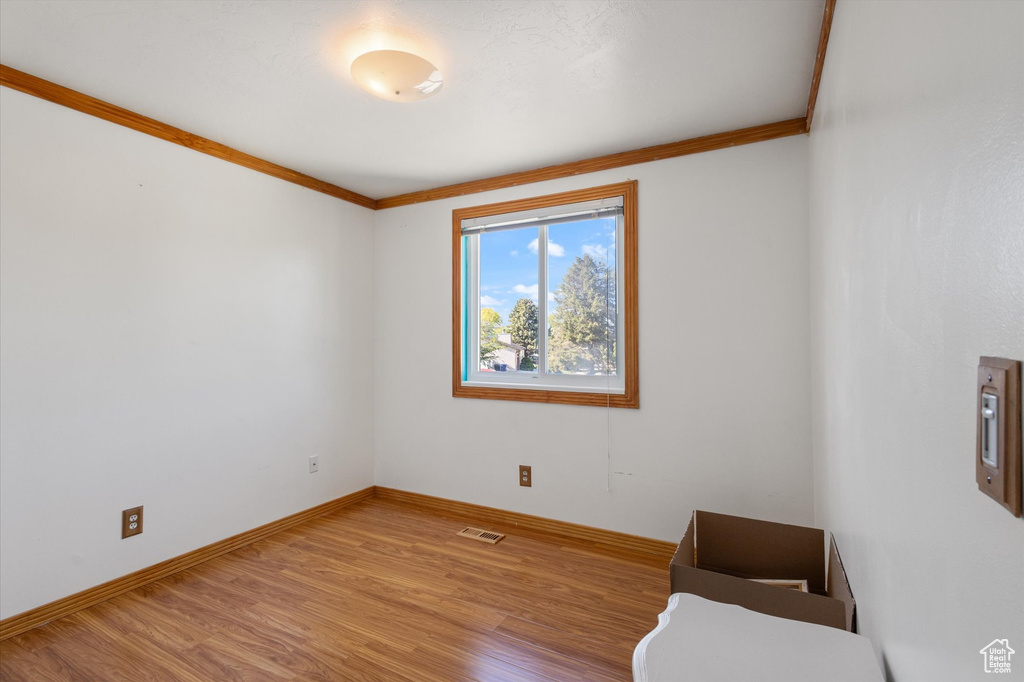 Spare room featuring baseboards, ornamental molding, visible vents, and wood finished floors